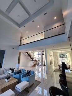 A glass railing with black cap runs along a second-floor balcony above a living room, with a mono stair beyond.