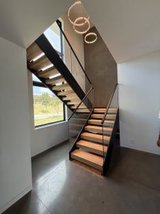 A black FLIGHT Duo switchback with oak treads and frameless glass rises past tall windows under ring pendants.
