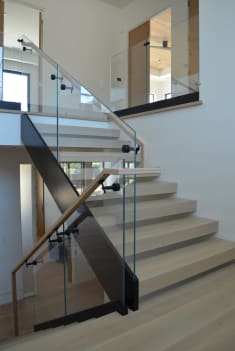 White oak stair along a black plate stringer with frameless glass and oak handrail rising from wide plinth steps.