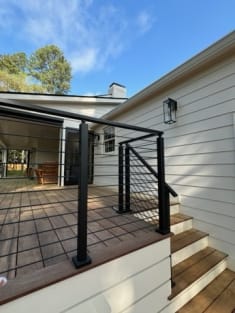 Black rod railing follows wood porch steps up to a covered patio on a white home.