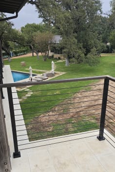 Black cable railing on a limestone terrace overlooking a pool and green lawn
