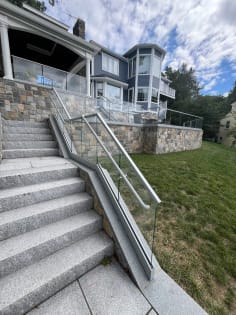 Full run of granite steps lined with glass base rail railing and a glass-mounted handrail below a stone terrace