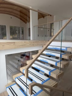 Floating wood treads with a glass railing and wood handrail rise to a glass-lined loft under a curved ceiling