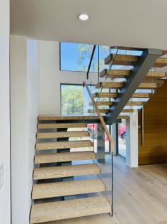 Switchback floating stair with thick ash treads, steel stringer and frameless glass railing in a sunlit entry
