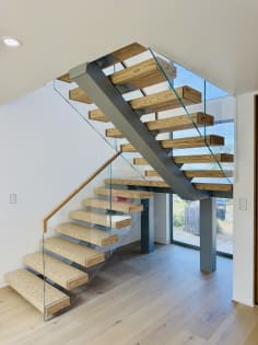 Floating ash treads on a dark steel mono stringer turn at a landing, edged with frameless glass and a wood handrail