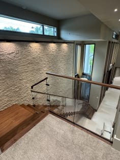 Glass railing with wood handrail at the top landing of a walnut stair beside a stone wall