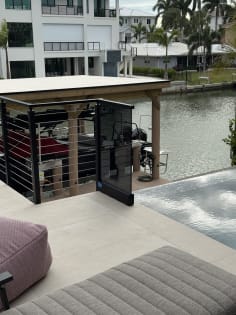 Solar gray glass panel and black cable railing beside a pool overlooking a canal and boathouse