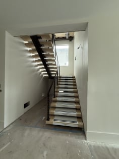 Black mono stringer switchback stair with white oak treads and black cable railing in a narrow stairwell