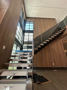 Floating stair with solar gray Vedera glass climbing a walnut-paneled wall beside tall windows