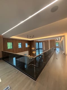 Solar gray base rail glass with a wood cap wraps a second-floor gallery under a glowing cove ceiling