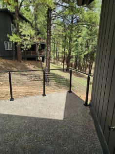 Black surface-mount cable railing along an aggregate patio overlooking a wooded slope