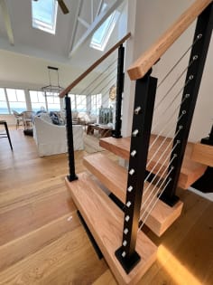 Red oak floating treads with black tread-mounted cable railing and oak handrail opening to a sunny living room