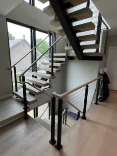 Pale oak FLIGHT Mono switchback on a black stringer with cable railing in a window-lit stairwell