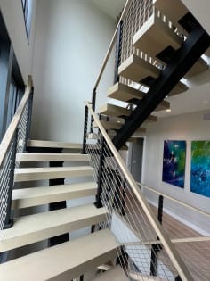 Whitewashed oak floating stair with cable railing beside colorful abstract art