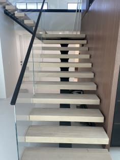 Long straight run of white oak floating treads on a black mono stringer with frameless glass and black handrail