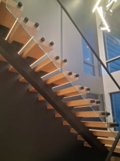White oak floating treads with LED strips on a black mono stringer beside frameless glass and a black handrail