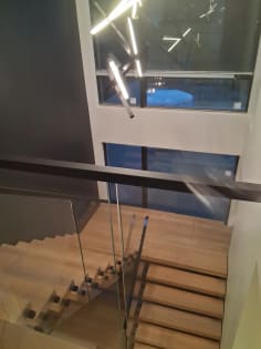 White oak floating switchback treads beside frameless standoff-pin glass and a black handrail