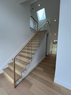 Frameless glass panels attached with round standoff pins and a wood handrail follow a white oak stair under a skylight.