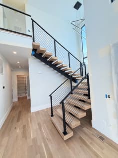 White oak floating treads on a black mono stringer switchback with black cable railing in a bright modern home.