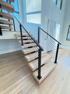Close view of white oak floating treads on a black mono stringer with black cable railing at the stair base.