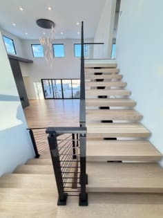 Open white oak treads on a mono stringer climb past a black cable railing toward a bright upper level.