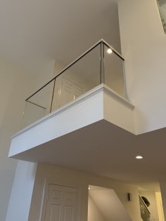 A frameless glass railing with slim cap tops a white interior balcony above a doorway.