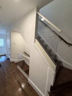 Frameless glass panel with white cap guards a dark-stained stair alongside a wall-mounted wood handrail.