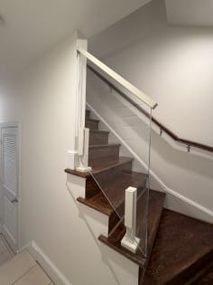 Frameless glass railing with a white cap rail beside a dark wood winder stair and wall handrail.