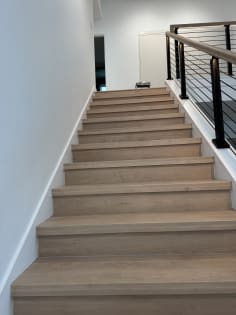 Light oak stair treads climb beside a black rod railing with wood handrail.