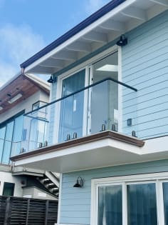 A cantilevered balcony with spigot-mounted glass and black top cap extends from a light blue clapboard home.