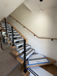 Viewrail-covered floating treads wind up beside a black-post cable railing and a wall-mounted oak handrail.
