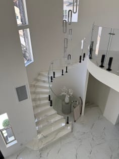 Curved glass railing on black talon clamps follows a white marble spiral stair under a crystal pendant.