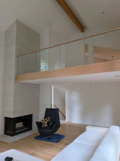 A wood-fascia loft lined with frameless hidden side-mount glass and an oak cap rail above a sitting area.