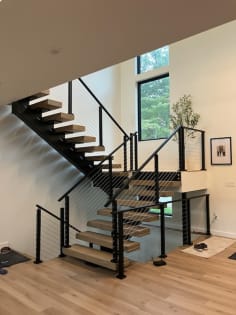Light oak treads on black mono stringers turning at a landing with black post cable railing.