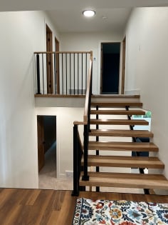 Hickory open treads on black stringers with black balusters and handrail rising to a balcony landing.