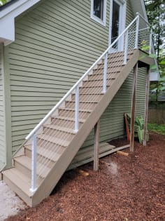 White posts and top rail with cable infill along a composite exterior stair beside sage-green siding.