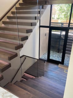 Walnut cantilevered treads turn at a landing beside frameless glass and wall handrail above a window to the garden.