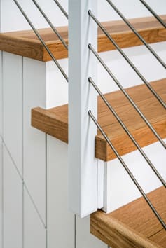 Close view of a white slim side-mount cable post fastened to a stair stringer with oak treads.