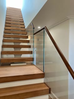 Oak floating treads rise beside frameless glass with a walnut handrail above closed lower steps.