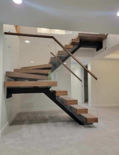 Walnut-toned treads on a black mono stringer turning through winders with a frameless glass railing and wood handrail.