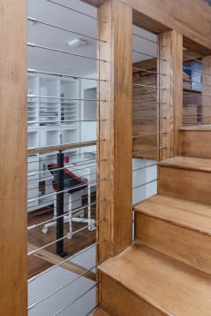 Stainless horizontal rods run between warm wood posts beside a natural wood stair.