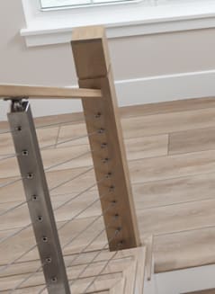 Close detail of a stainless cable post meeting a square wood newel with wood handrail.