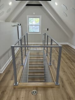 Symmetric view of a stair opening framed by silver cable railing in a vaulted attic room.