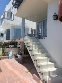 Clear glass on bronze standoff pins guards a white exterior stair beside a tiled patio.