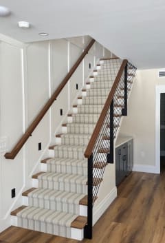 Black side-mount posts with rod infill and a walnut handrail along a stair with a striped runner.