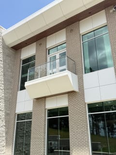 Post-to-post glass railing on a white cantilevered balcony set into a brick and stone office facade.