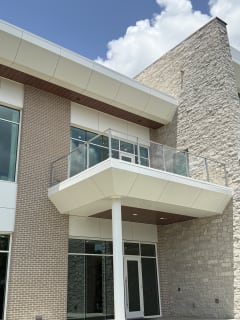 Post-to-post glass railing on a white cantilevered balcony above the entrance of a brick and stone office building.