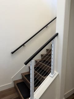 Bright white cable posts with a black top rail and matching wall handrail along an interior stair.