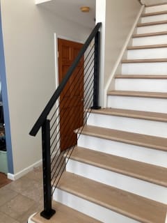 Black posts and handrail with horizontal Onyx rods follow a white stair with light wood treads.