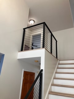 Black Onyx rod railing guards an upper landing and follows the stair in a bright split-level hallway.
